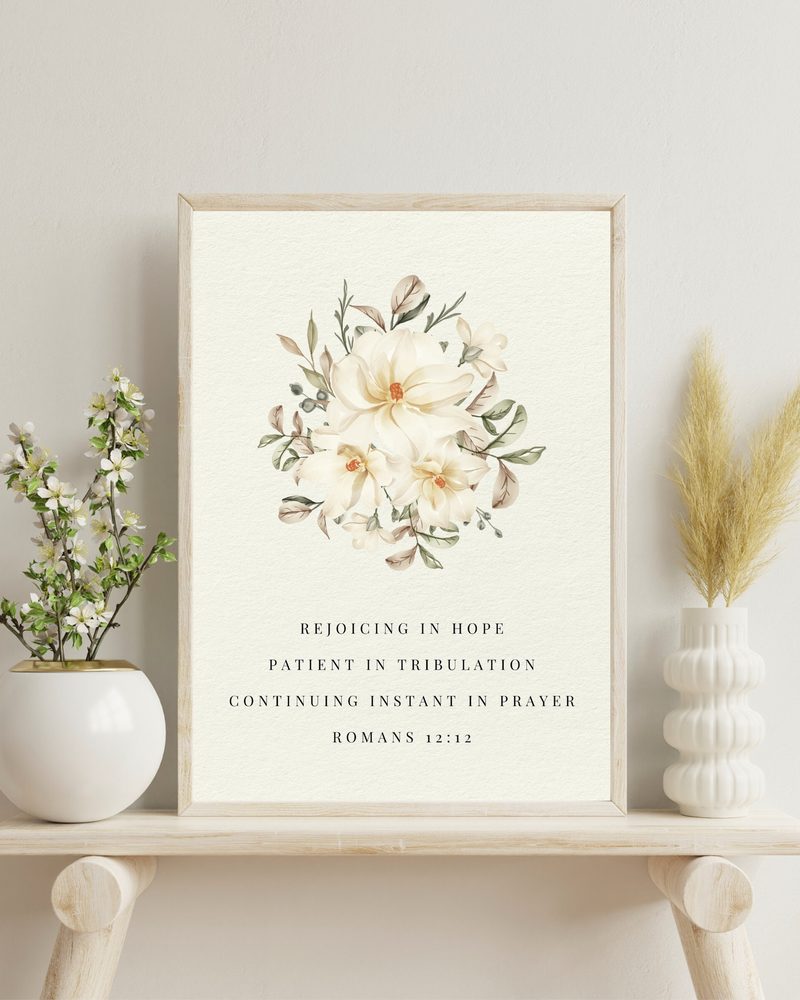 Romans 12:12 KJV floral wall art — the sheet in a light wood frame, on a shelf with blossom
